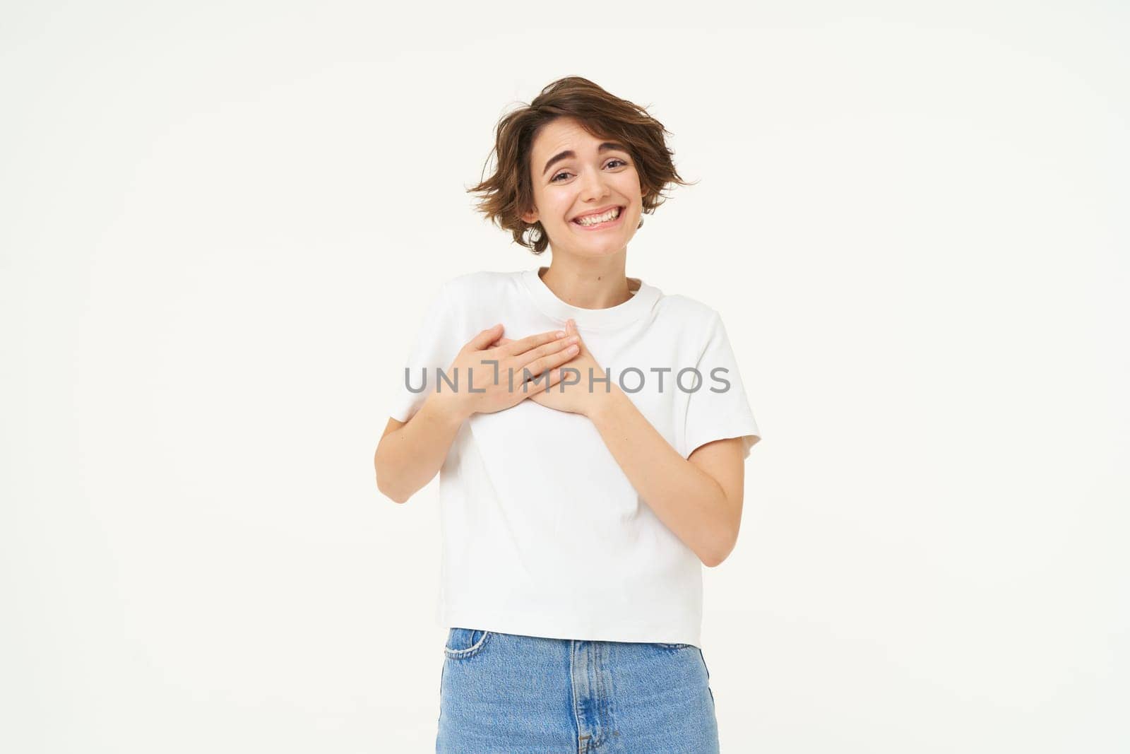 Portrait of woman expressing care, self-love and caring emotions, holds hands on chest, looking with smile at camera, isolated over white background by Benzoix