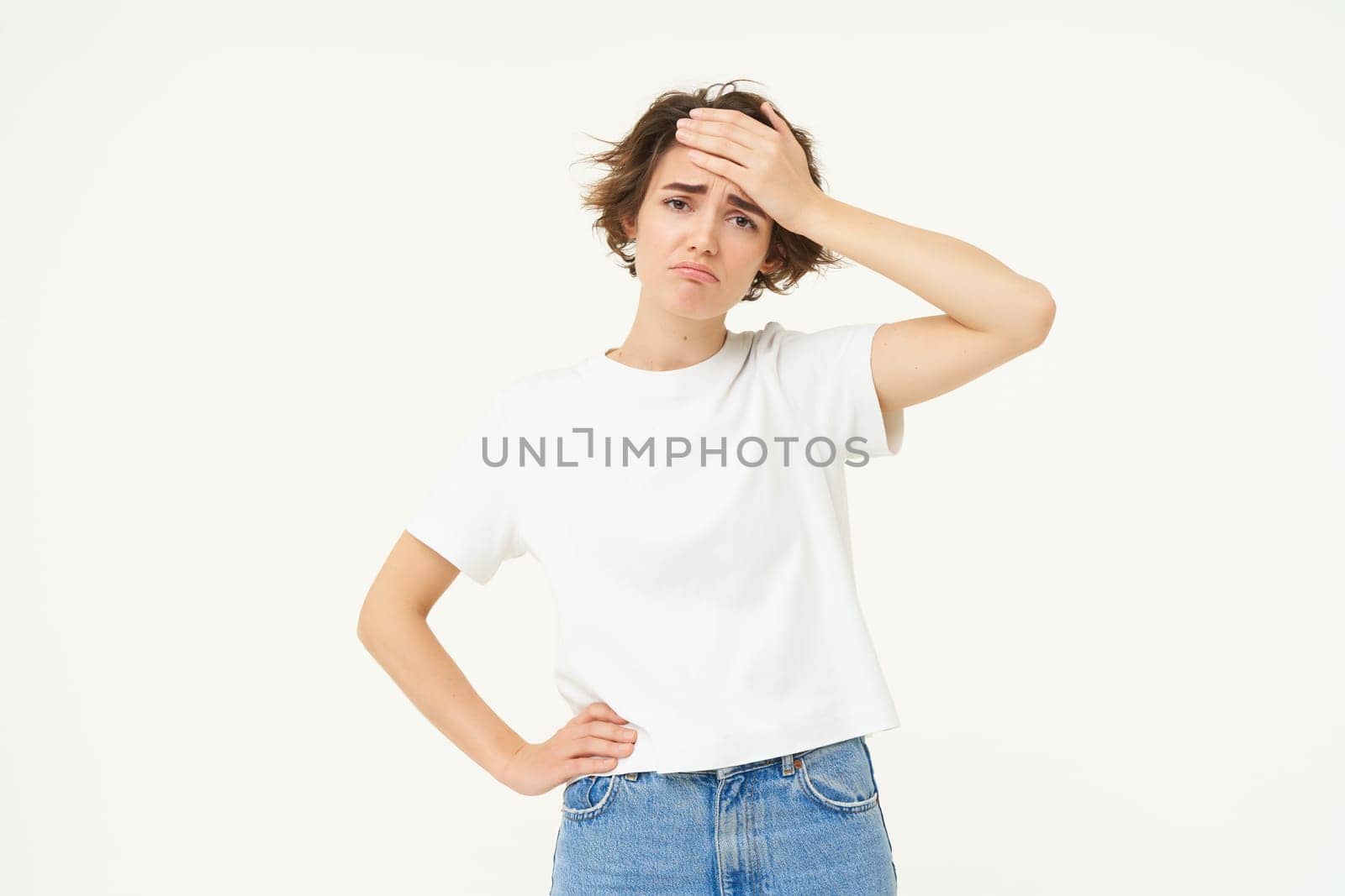 Portrait of woman with headache, touches her forehead, has temperature, high fever, feeling unwell, looking sad, standing over white background.