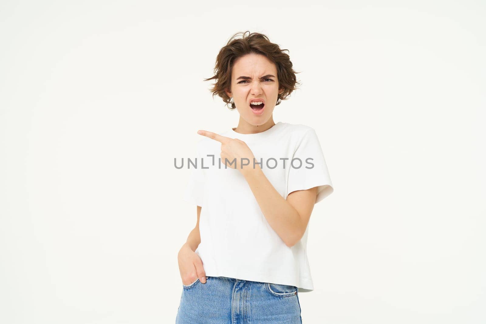 Portrait of woman complaining, pointing finger left, looking disappointed and upset, standing over white studio background.