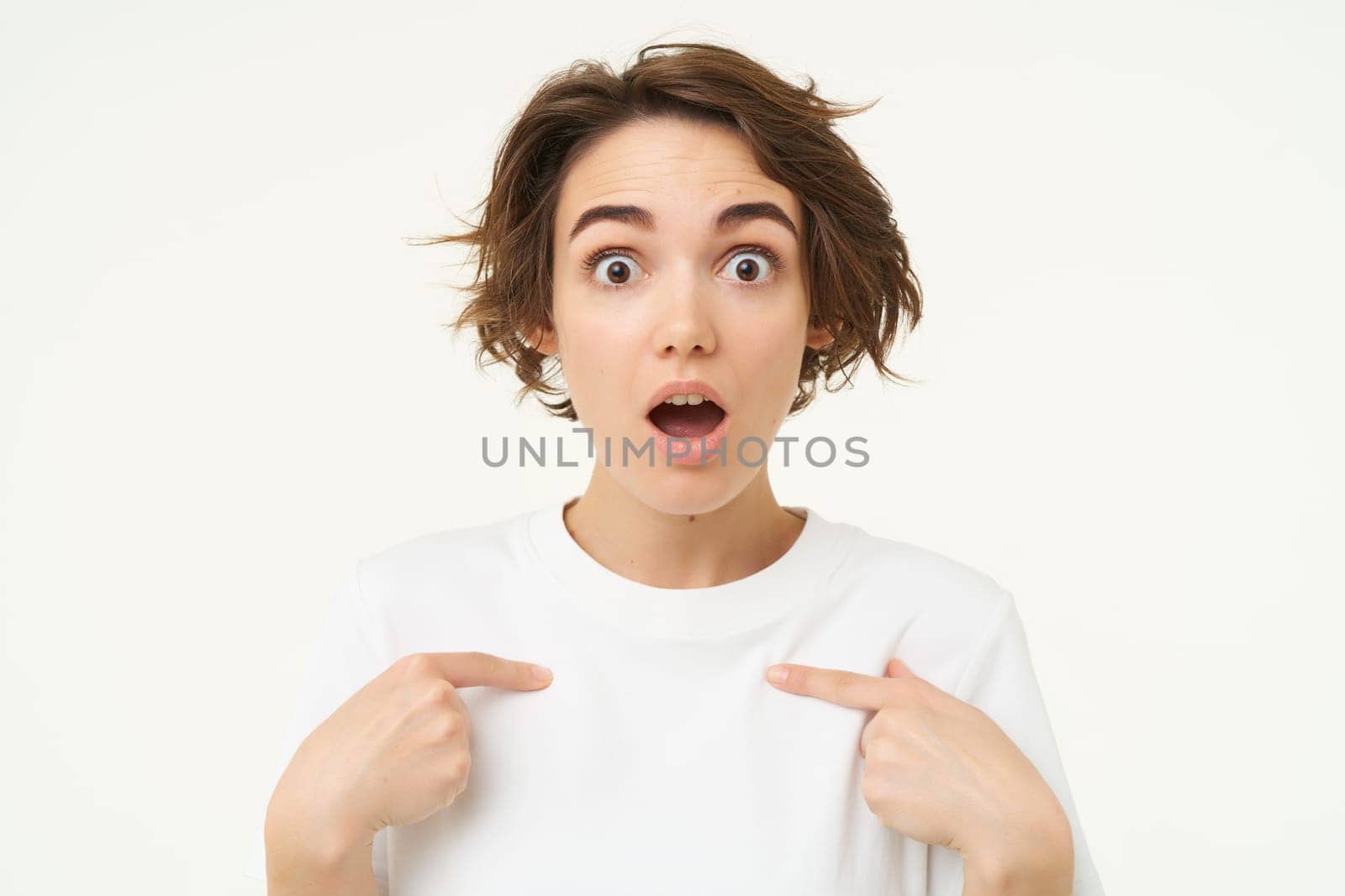 Close up portrait of girl with surprised face, points at herself, looks shocked, stands over white background by Benzoix