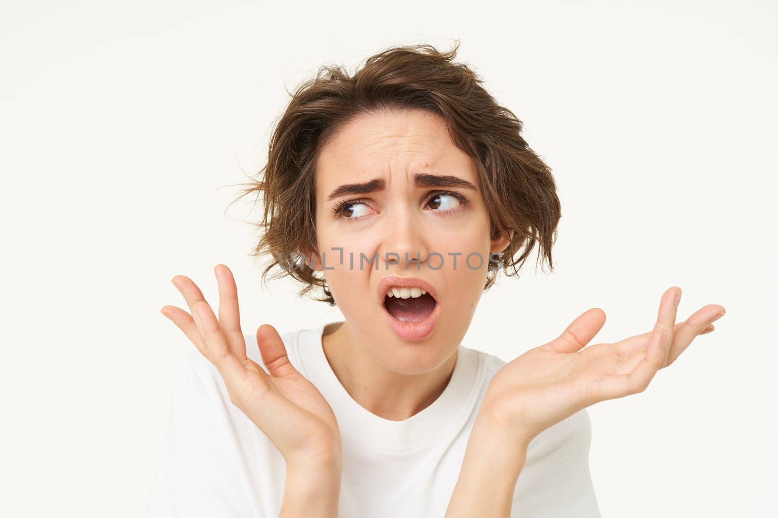 Portrait of confused, puzzled young woman, gasping, looking disappointed and frustrated, shrugging shoulders, posing over white background.