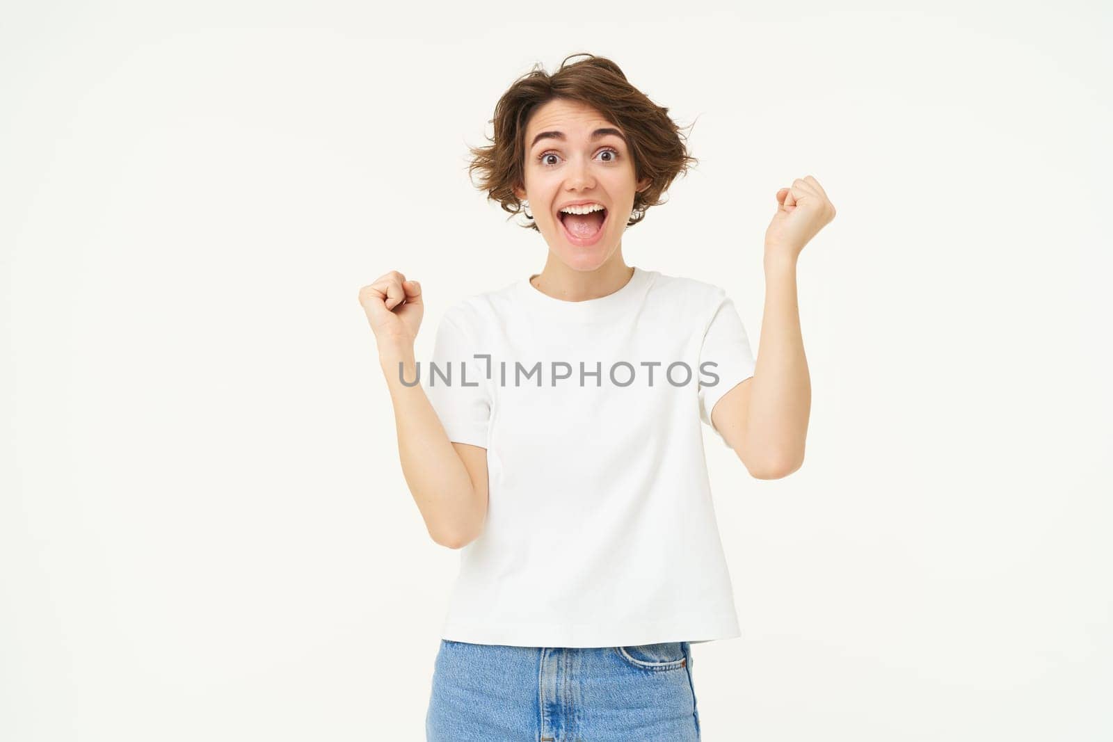 Portrait of happy, excited young woman winning, triumphing, feeling like champion, posing over white background.