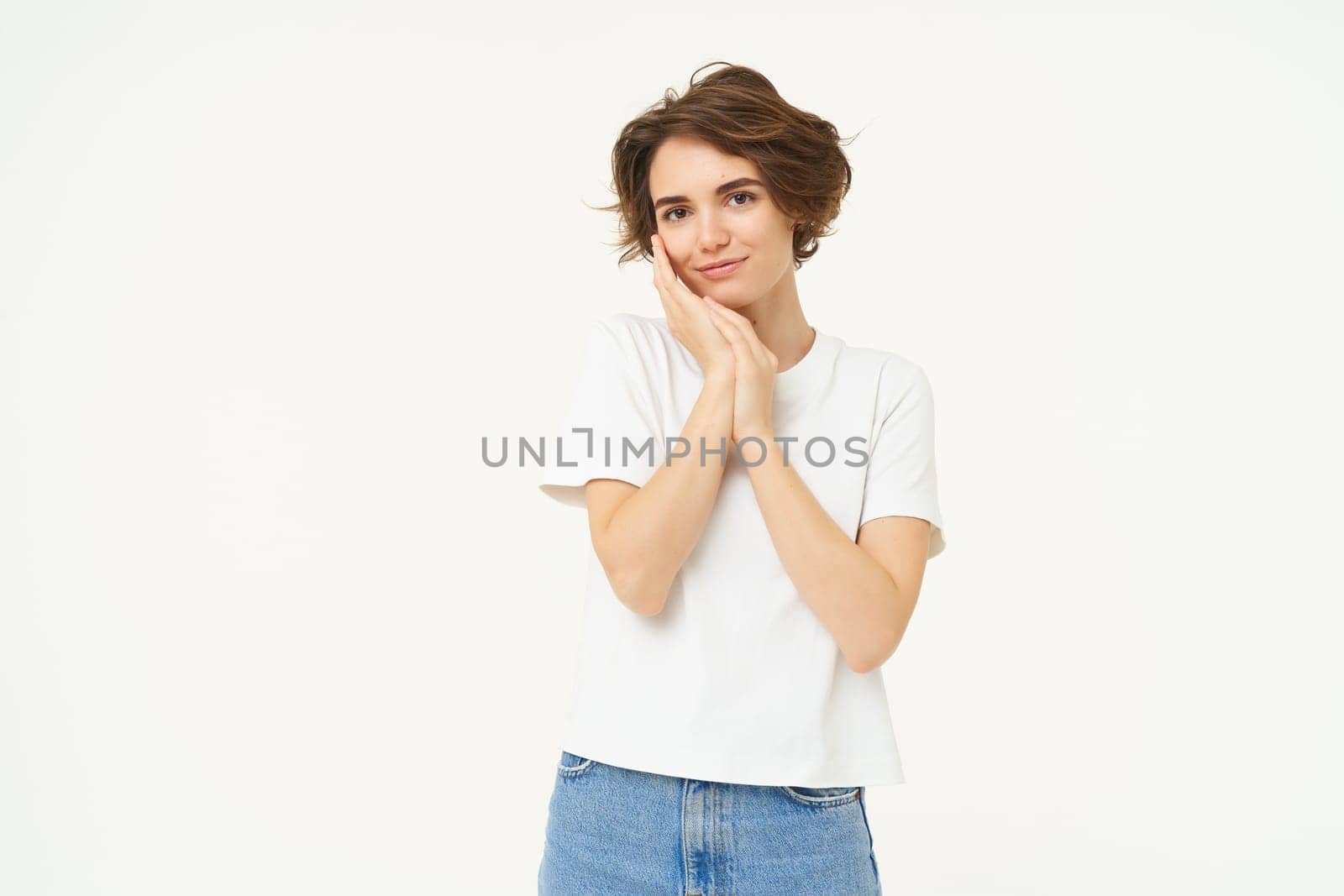 People and lifestyle. Portrait of smiling, gentle young brunette woman, gazing at camera, looking at something lovely, standing over white studio background.