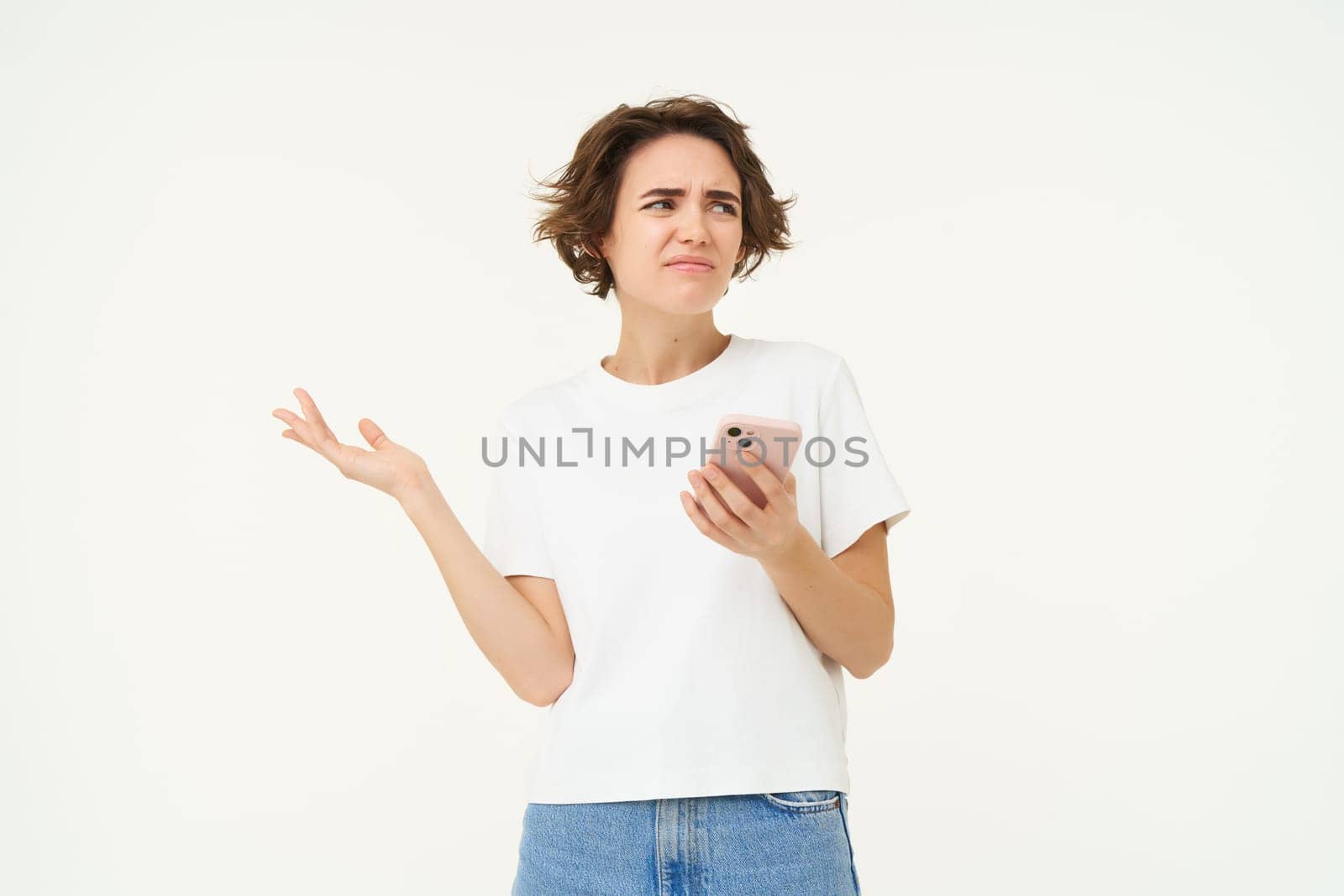 Portrait of woman with smartphone standing confused, puzzled, cant understand something online, using mobile phone, posing over white studio background by Benzoix