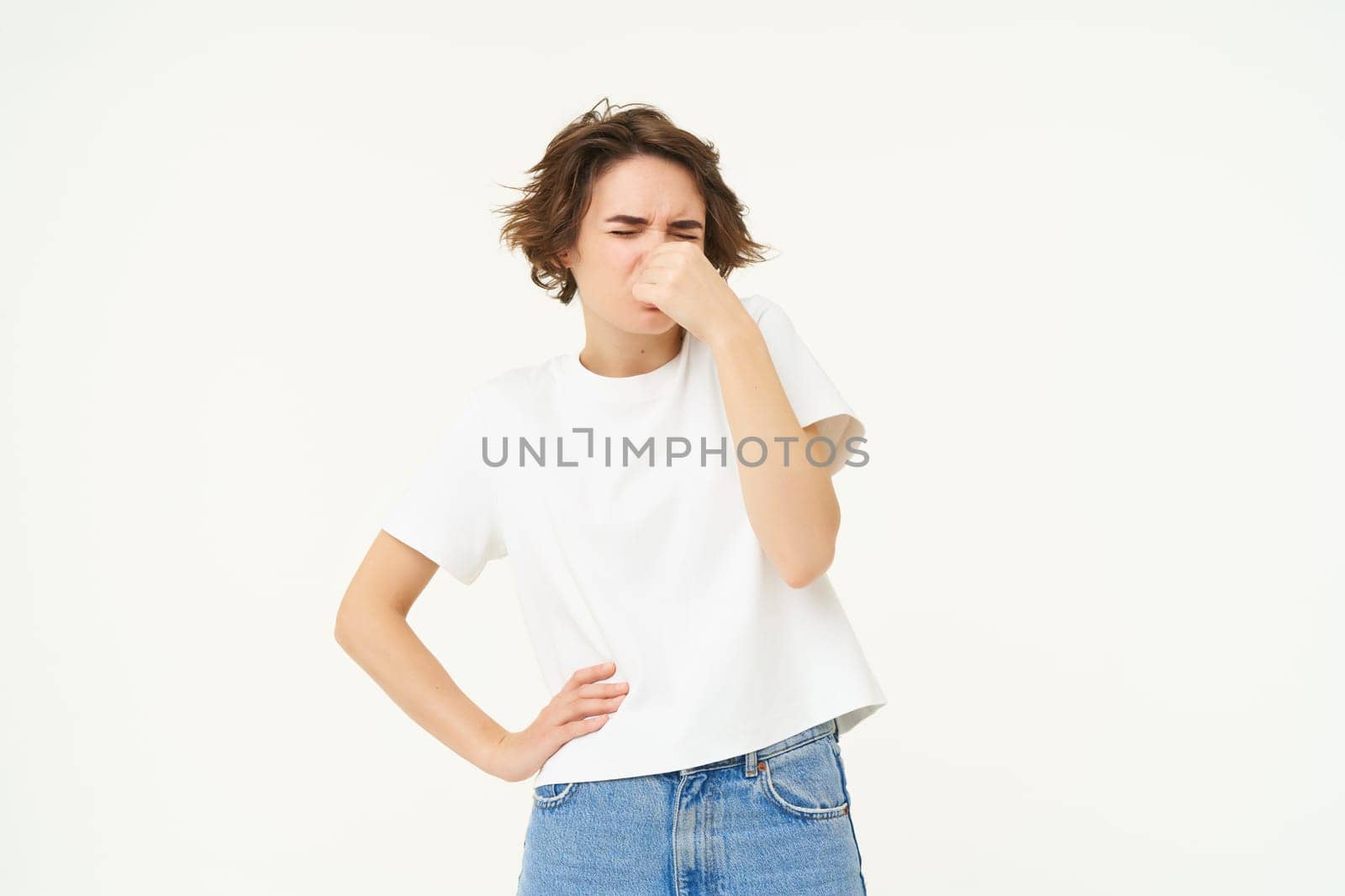 Portrait of woman that shuts her nose from awful, disgusting smell, something stinks, stands over white background. Copy space