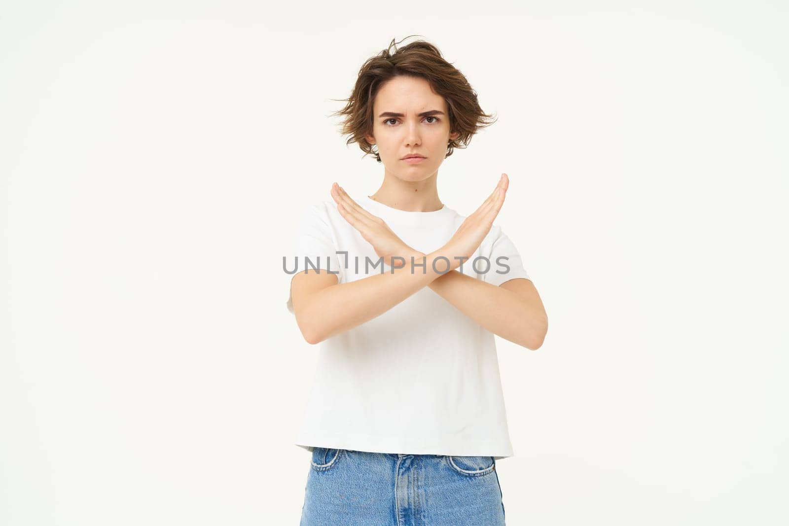 Portrait of woman with serious face, shows cross, stop gesture, prohibit something bad, standing over white background. copy space