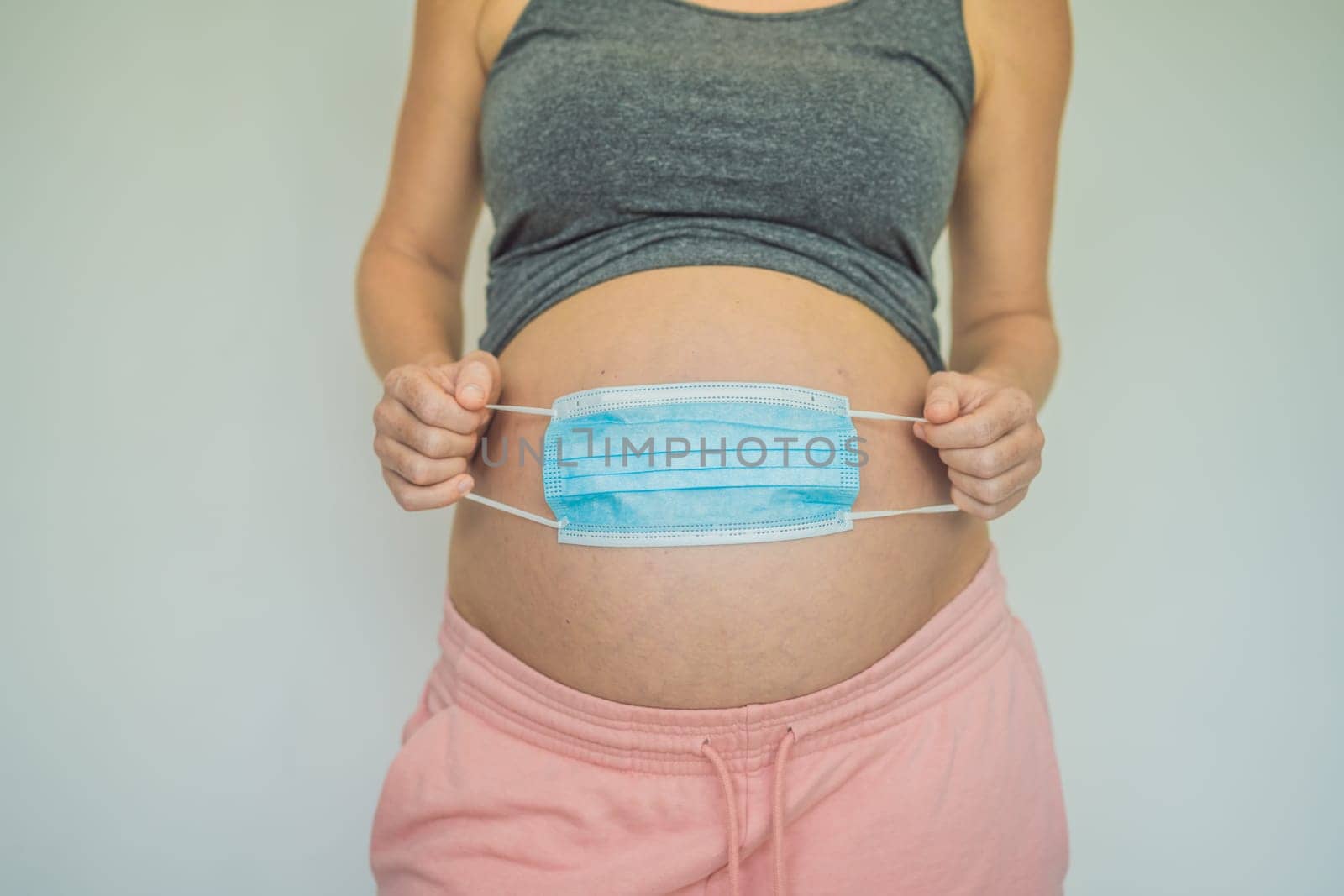 Belly of a pregnant woman holding medical mask close up.