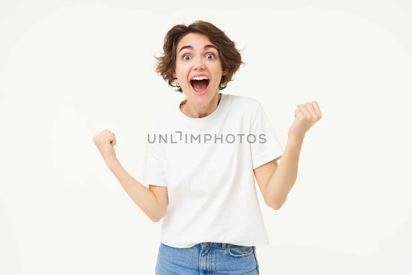 Portrait of happy, excited young woman winning, triumphing, feeling like champion, posing over white background.