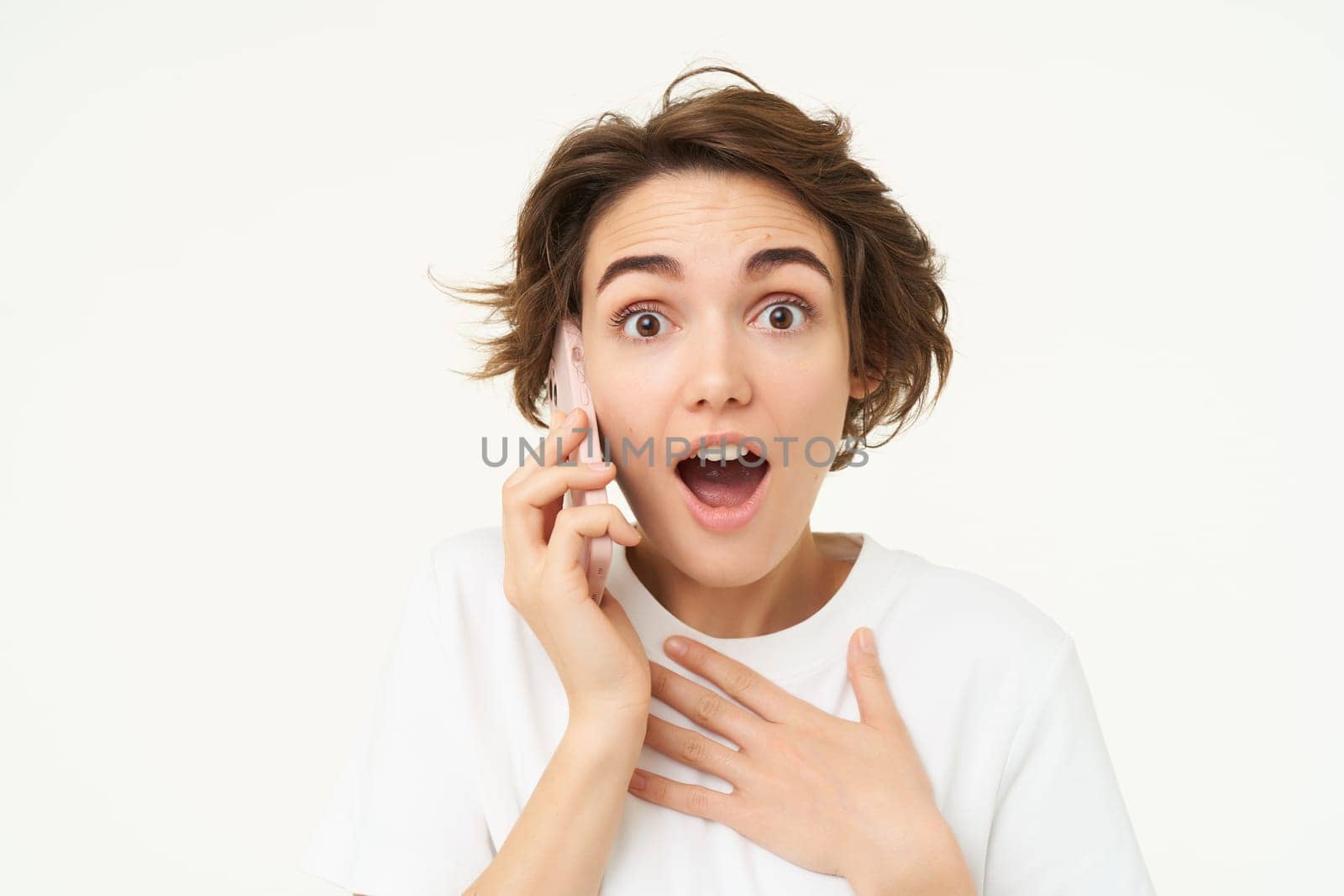 Portrait of woman with surprised face, answers phone call and looks excited, amazed by big news, stands over white background.