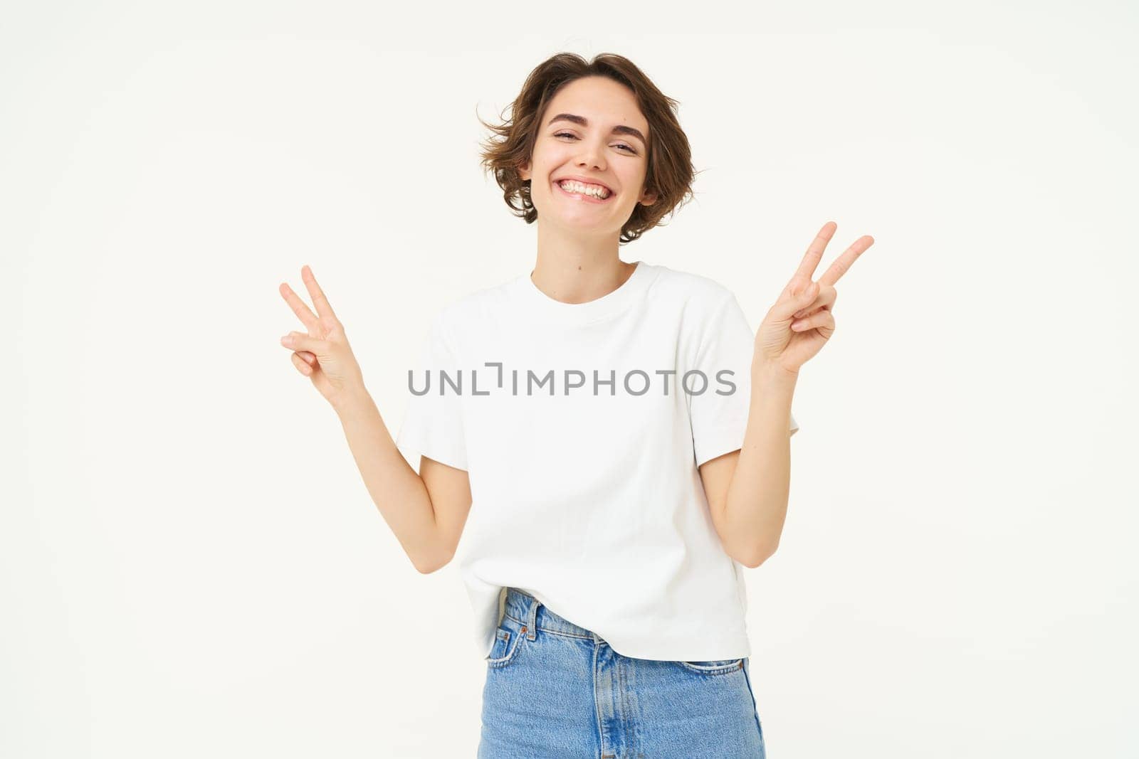 Portrait of happy and carefree woman, shows peace, v-sign gesture, having fun, posing for photo over white background.