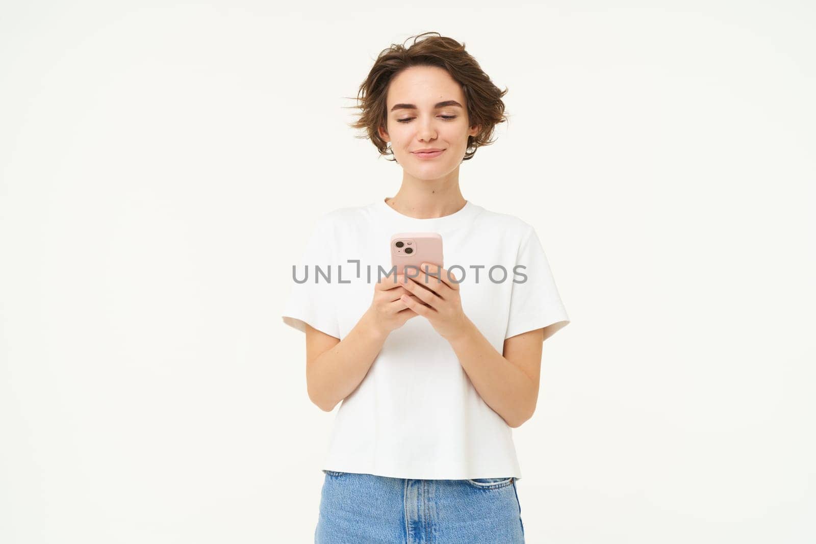 Portrait of brunette woman using smartphone, standing with mobile phone, texting, placing an order, browsing social media in telephone, standing over white background.