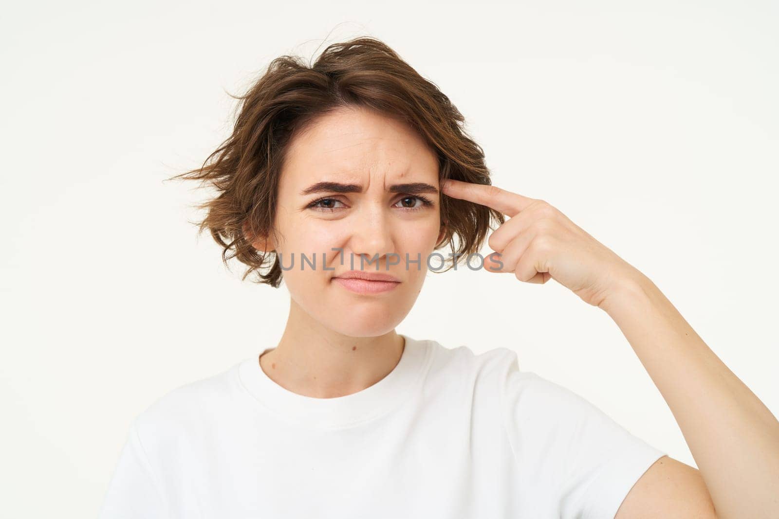 Young woman rolling finger on forehead and looking with disappointment, thinks someone is stupid or crazy, isolated over white background.