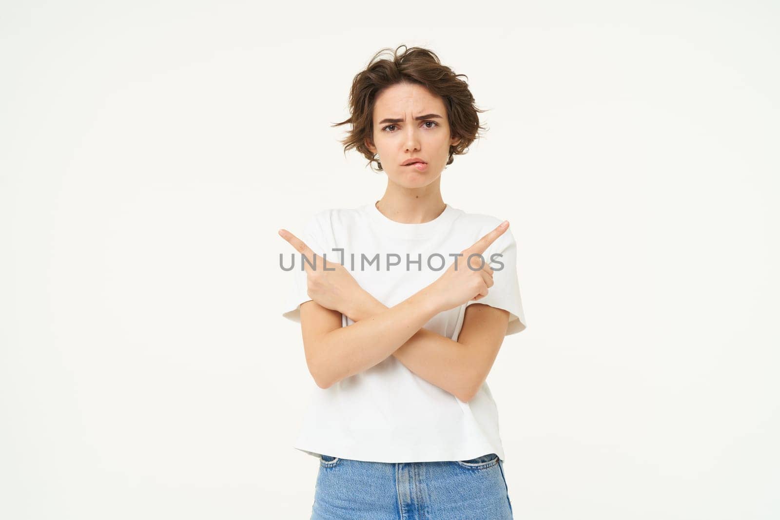 Portrait of sad, frowning woman, pointing sideways, making complex decision, difficult choice, isolated over white background. Copy space