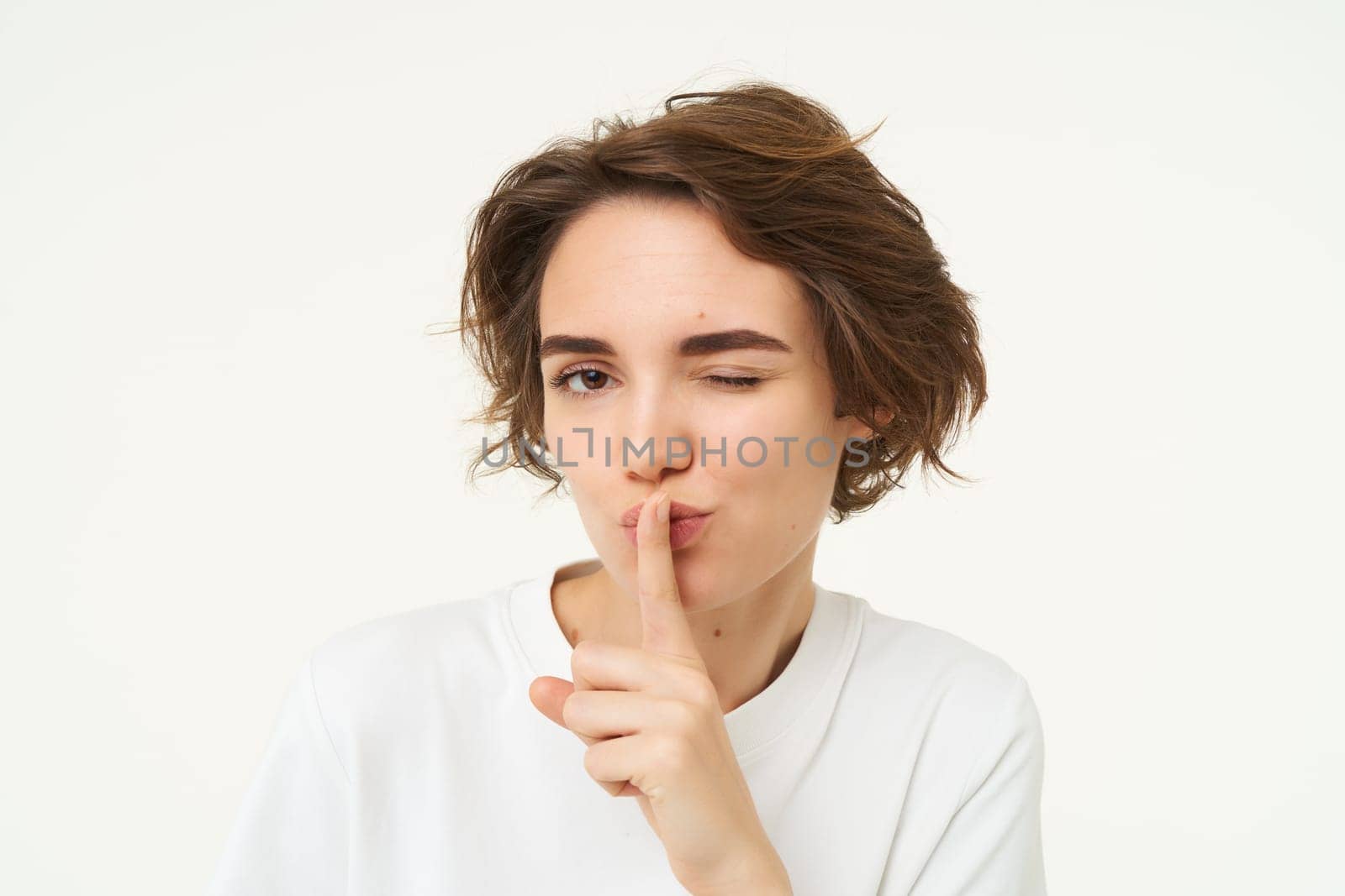 Close up shot of cute girl, press finger to lips, makes shhh shush noise, keeps secret, stands over white background.