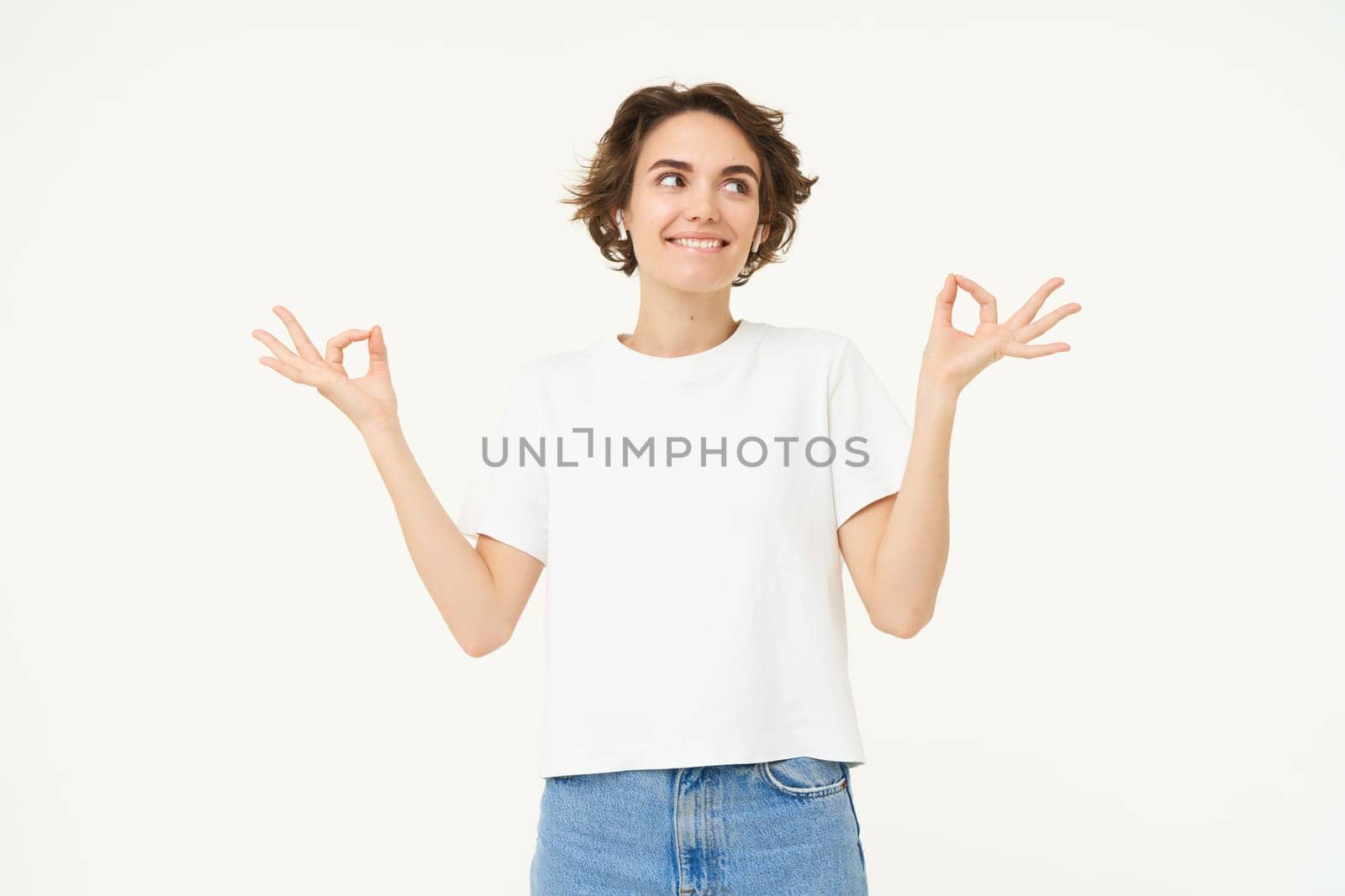 Portrait of young girl feeling happy and positive, meditating, holding hands sideways in zen, practice yoga, standing over white background. Copy space