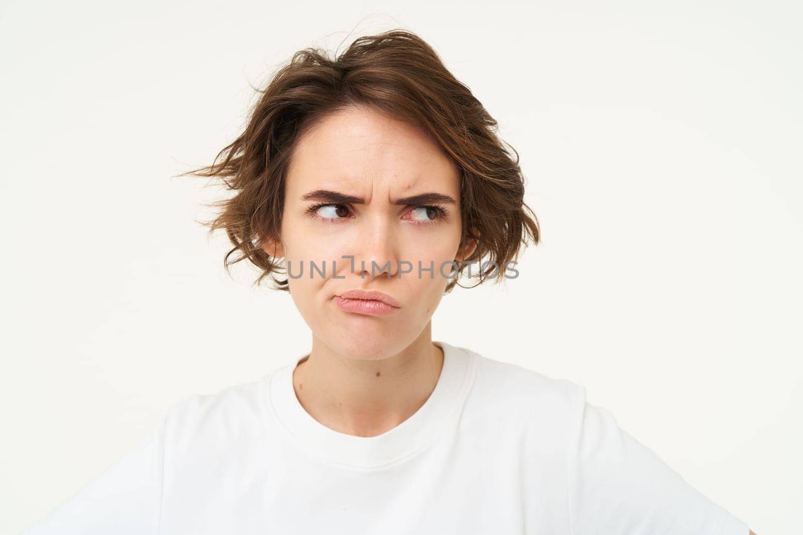 Portrait of frowning, grumpy young woman, looks upset and offended, disappointed by something, standing over white background. Copy space
