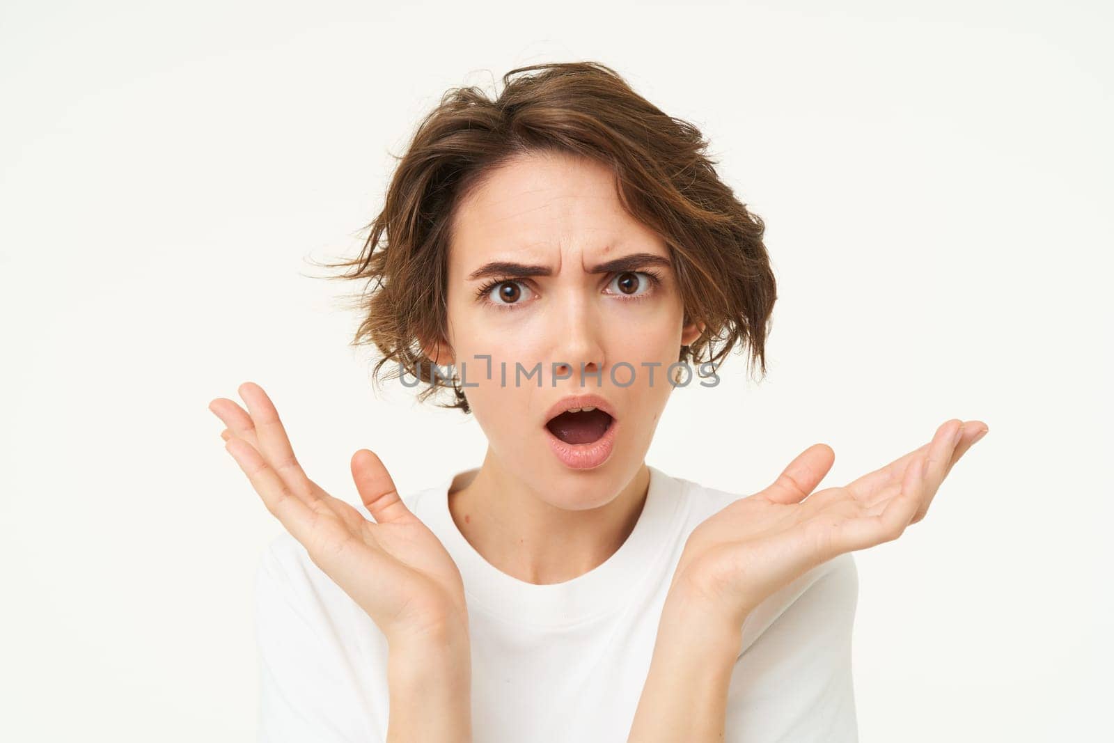 Close up of shocked brunette woman, shrugging and looking disappointed, posing over white studio background by Benzoix