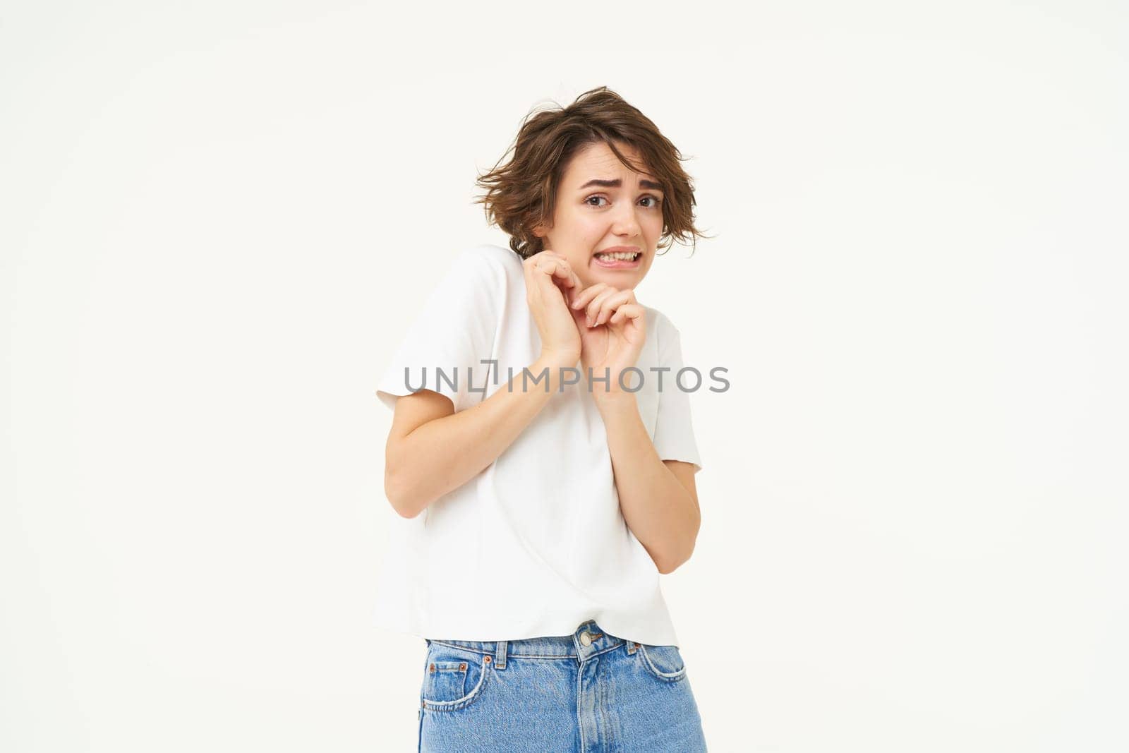 Image of girl jumps from fear, scared, looking frightened, standing against white studio background. Copy space