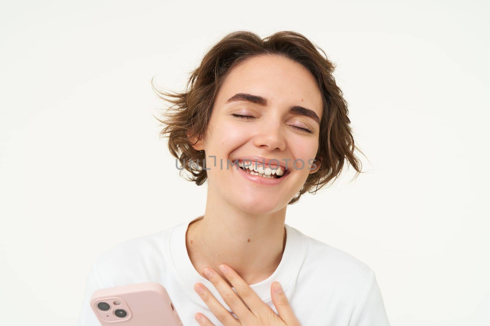 Portrait of young woman standing with pink mobile phone, using smartphone app, doing online shopping, paying for something using application, standing over white background.