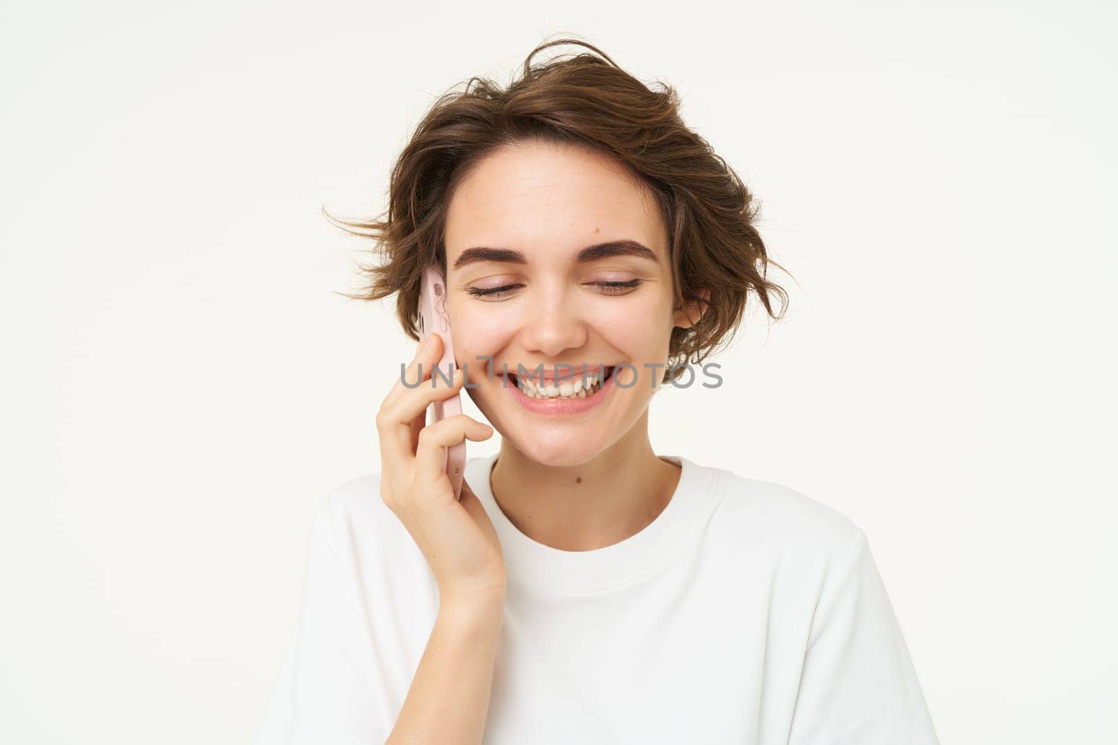 Image of smiling, brunette woman calling someone, talking on mobile phone, answer telephone call, standing over white background.