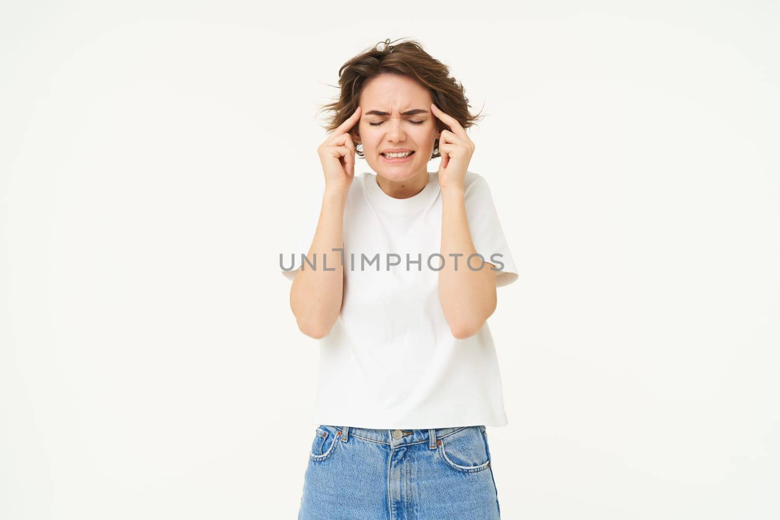 Image of distressed, upset young woman touches her head, has headache, suffers from migraine, stands over white background by Benzoix