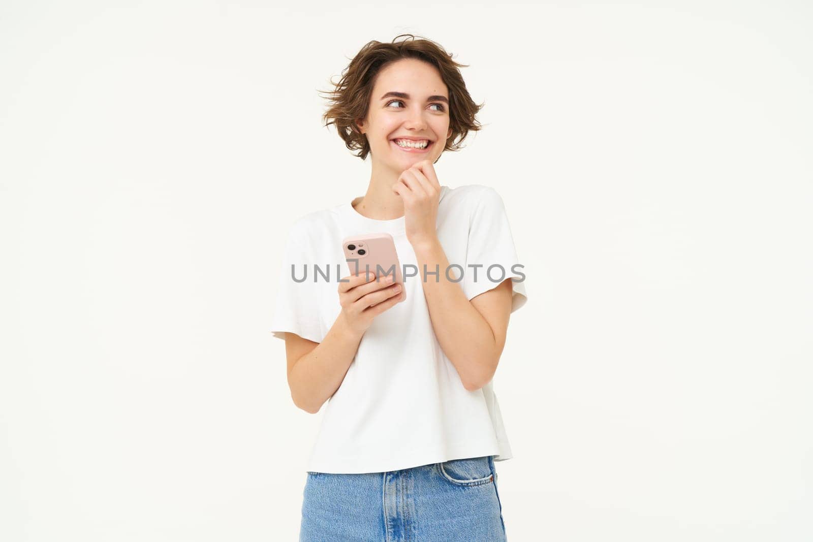 Portrait of brunette girl laughing, holding smartphone and giggle from something funny, posing over white studio background. Technology concept