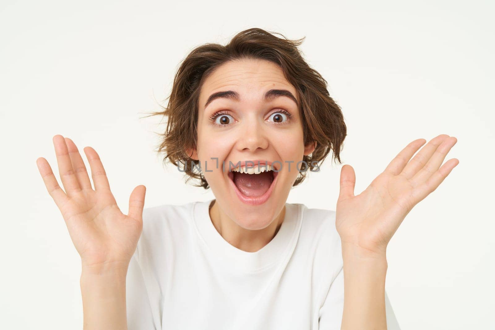 Close up portrait of excited brunette woman, gasping and smiling, claps hands and looks amazed, stands over white background.