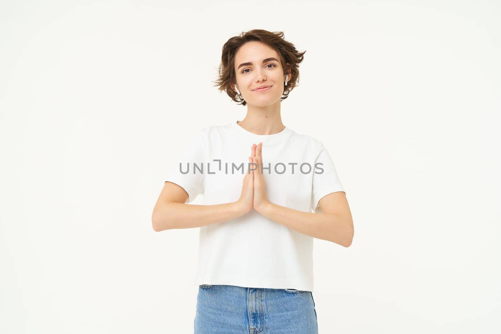 Portrait of mindful young woman, showing namaste, grateful gesture, saying thank you, asking for something and smiling, standing over white background by Benzoix