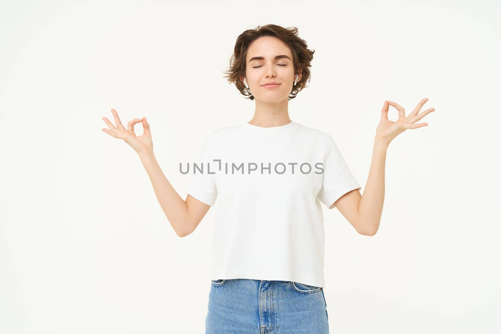 Portrait of young woman feeling peace and relaxation, holding hands sideways, zen gesture, meditating, practice mindfulness yoga, standing over white background.