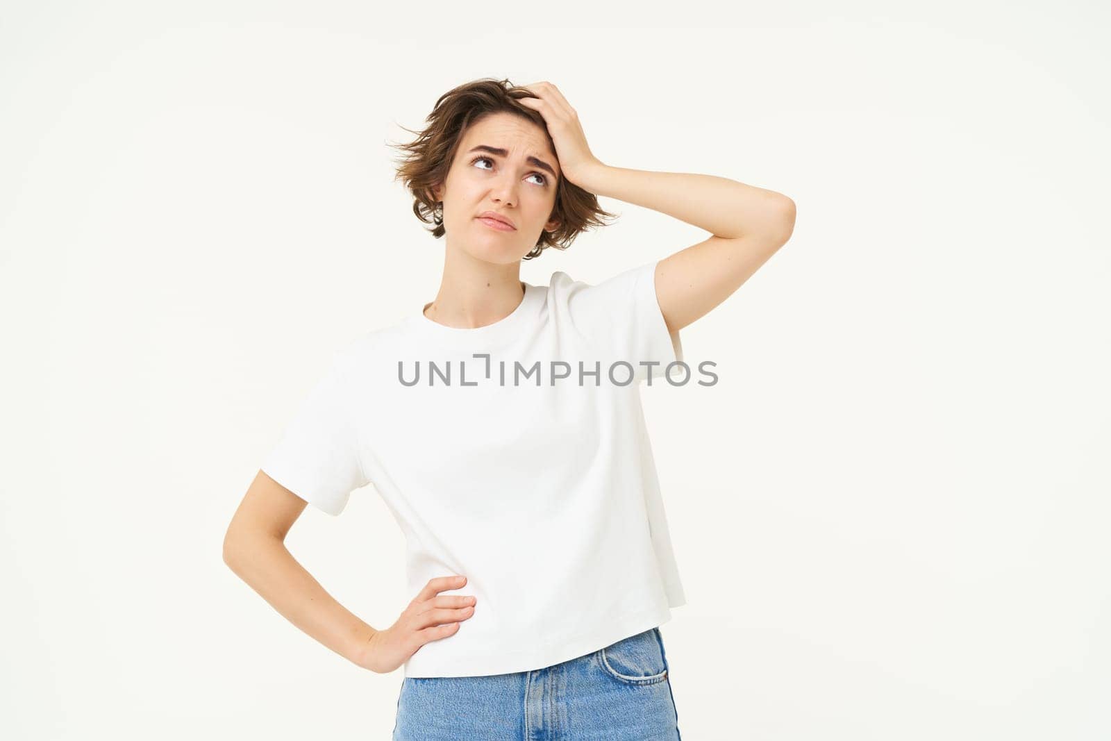 Portrait of woman looking troubled, slap her forehead, standing thoughtful and frowning, facing complicated problem, standing over white studio background.