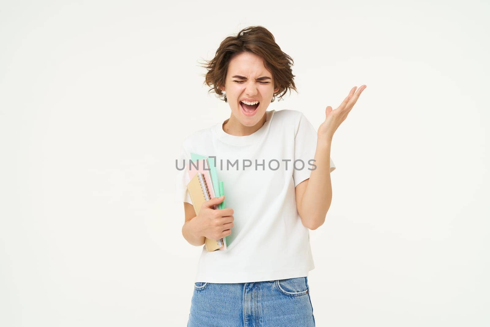 Stressed young girl student, woman screams, stands with notebooks and folders, looks depressed, stands over white background.