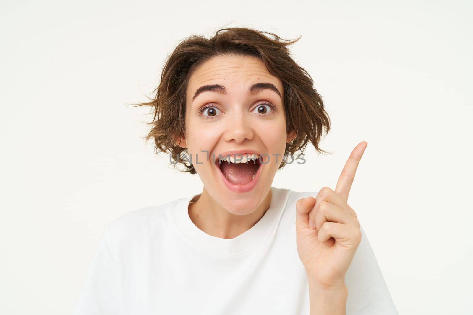 Close up of excited smiling woman, pointing finger up, showing number one, has an idea, thinking of a plan or solution, standing over white background by Benzoix