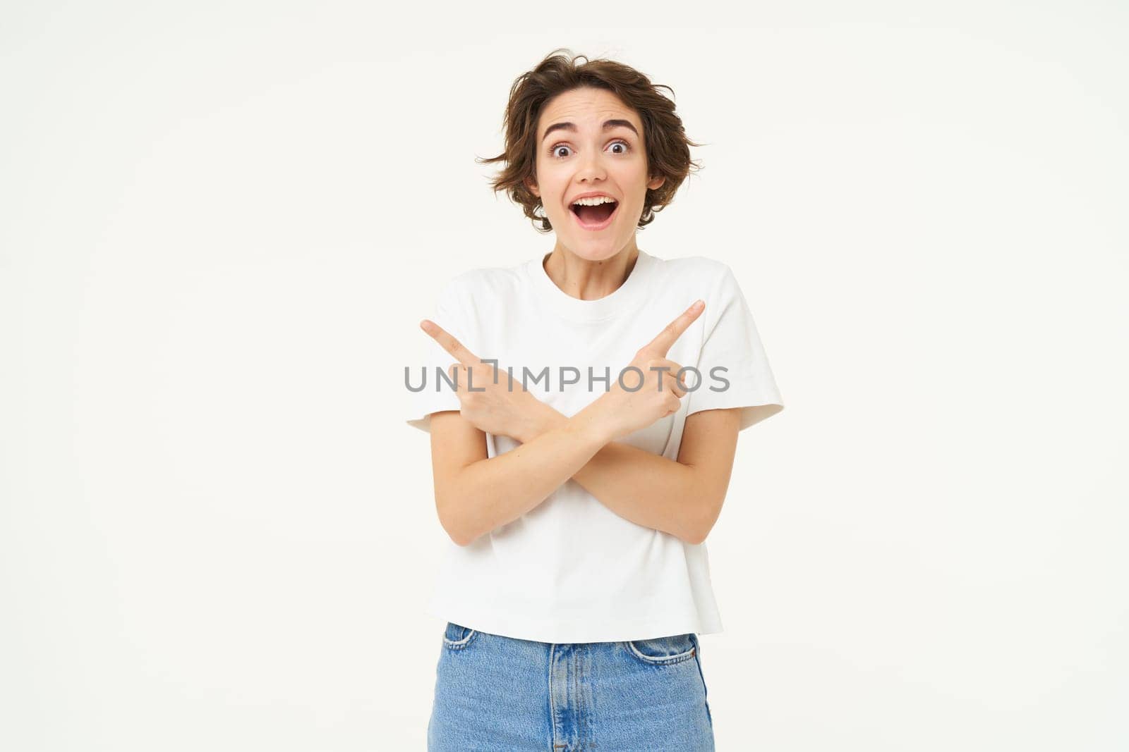Portrait of amazed, happy young woman pointing sideways, left and right direction, showing advertisement, two choices, standing over white studio background.