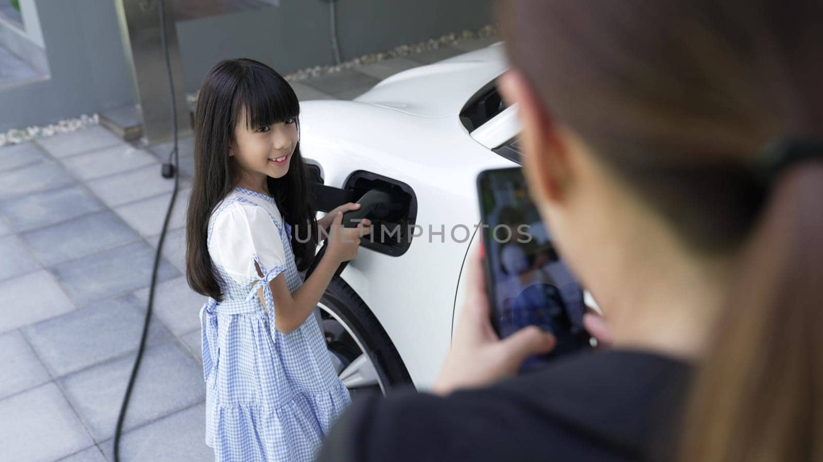 Progressive lifestyle of mother and daughter who have just returned from school in an electric vehicle that is being charged at home. Electric vehicle powered by sustainable clean energy.