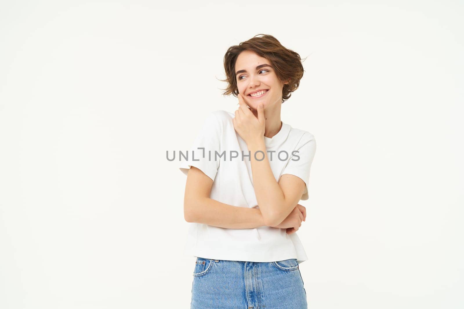 Portrait of young woman in casual clothes, laughing and smiling, touching her face without blemishes, standing over white background. Copy space