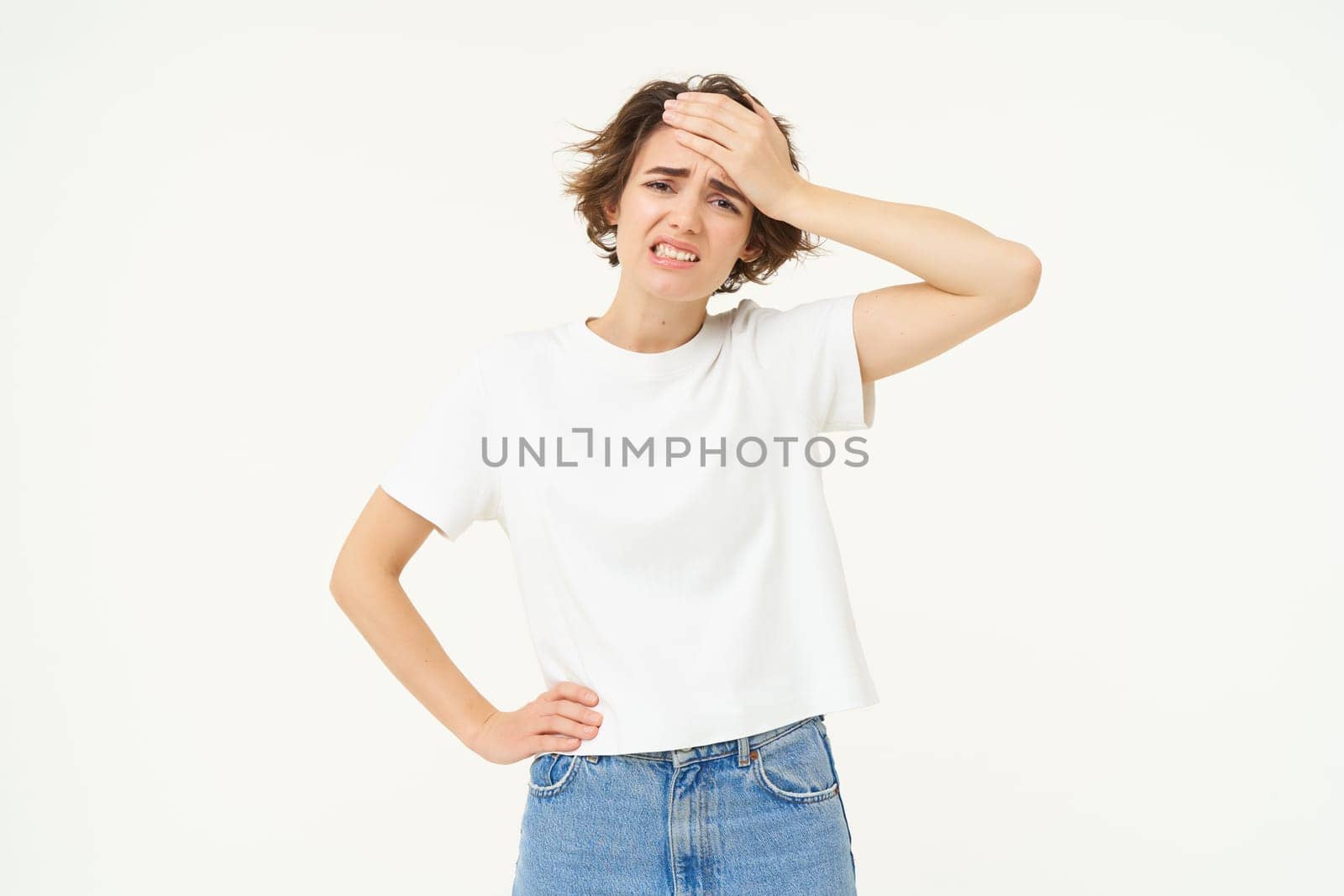 Image of woman with troubled face, holds hand on forehead, frowning and looking worried, forget something, standing over white background.
