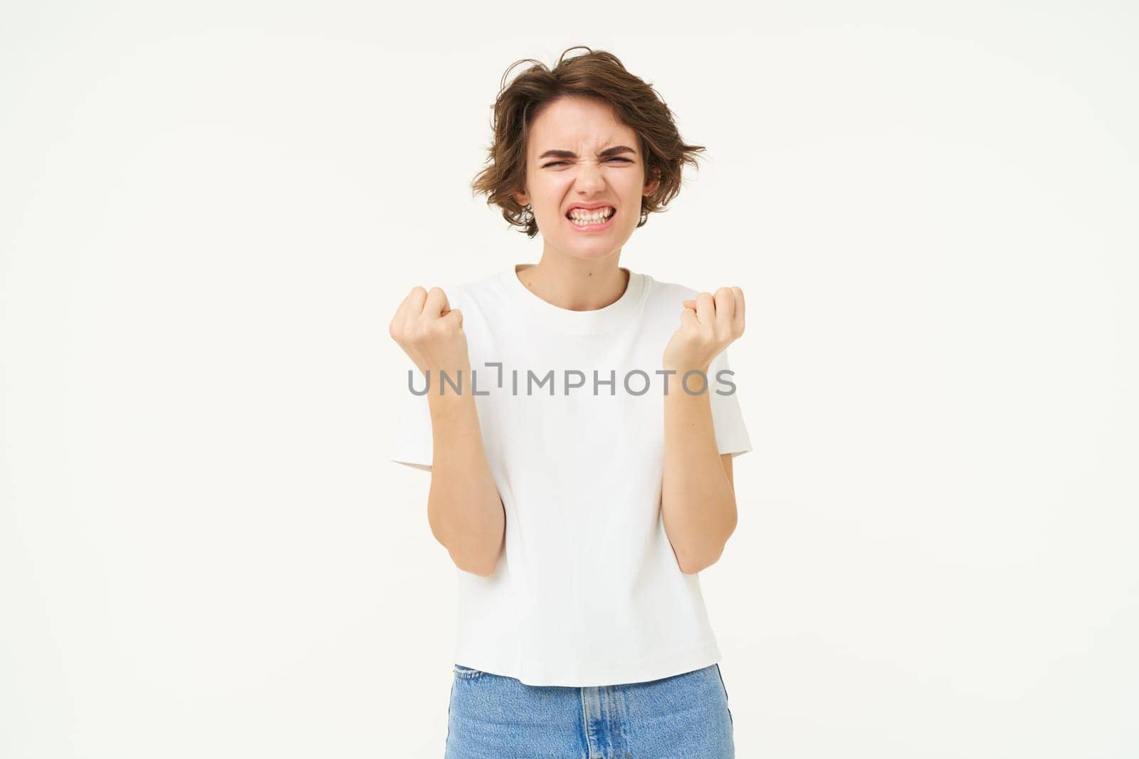Portrait of confident and motivated woman, clenches her fists and looks self-assured, stands over white background. Copy space