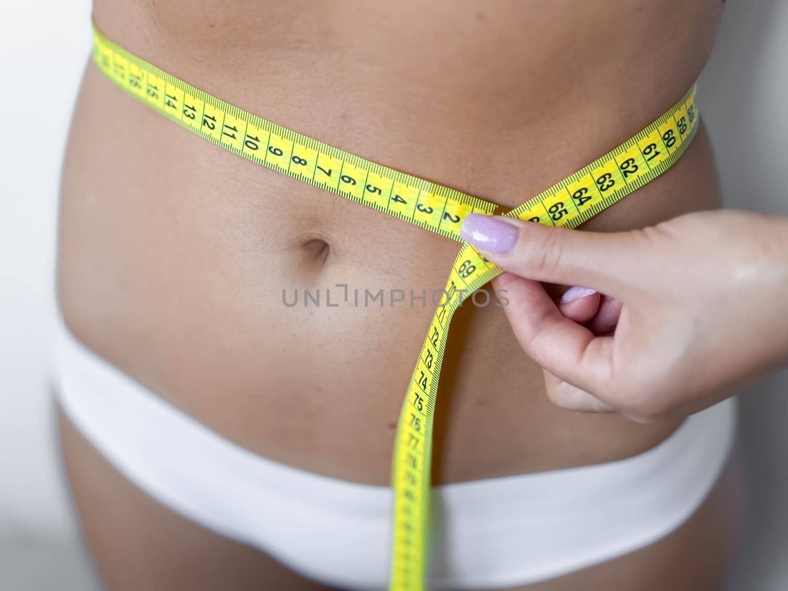 Measuring waist with tape for fitness and health monitoring.