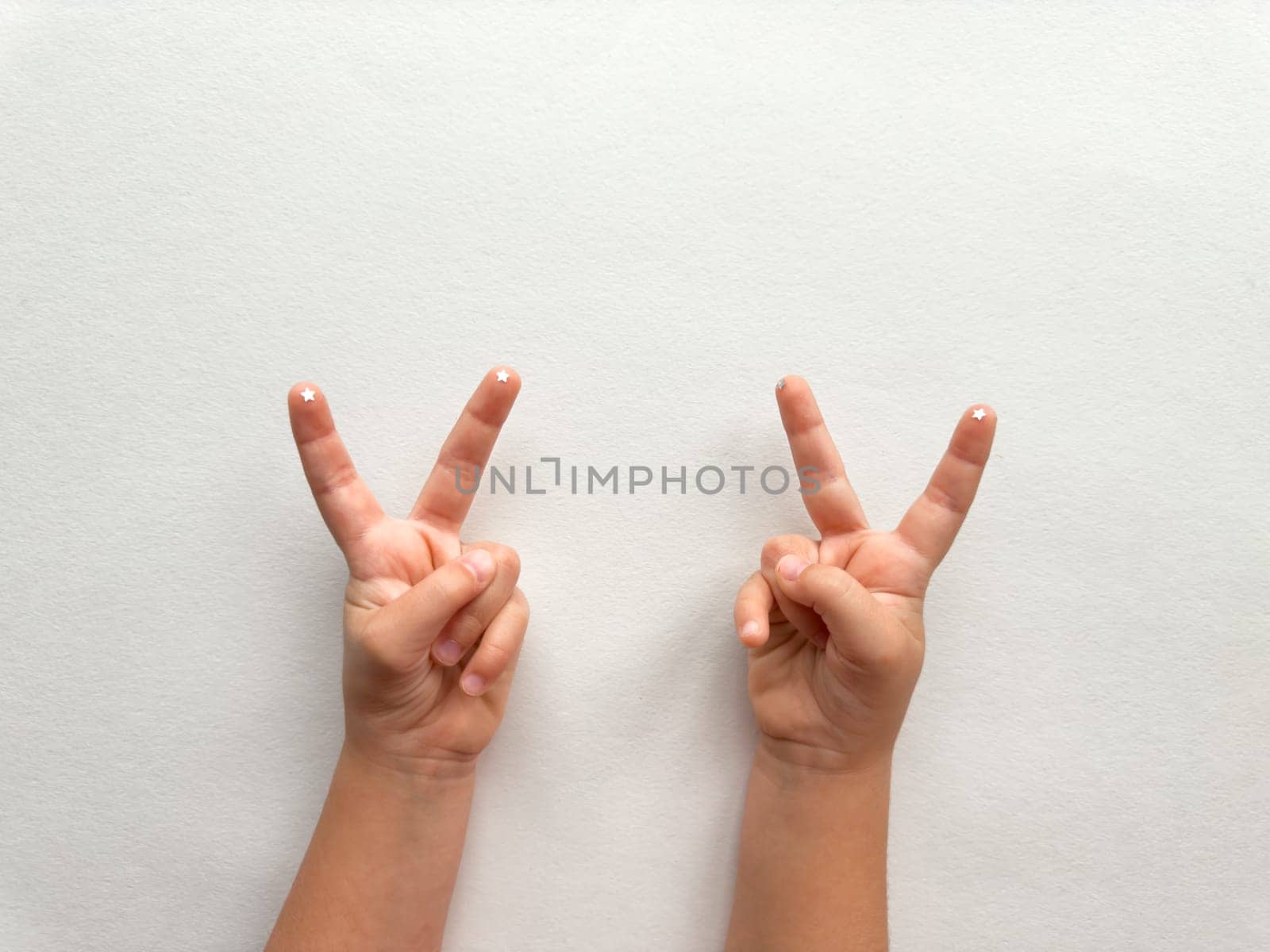 Childs hands showing peace sign on minimalist white background.