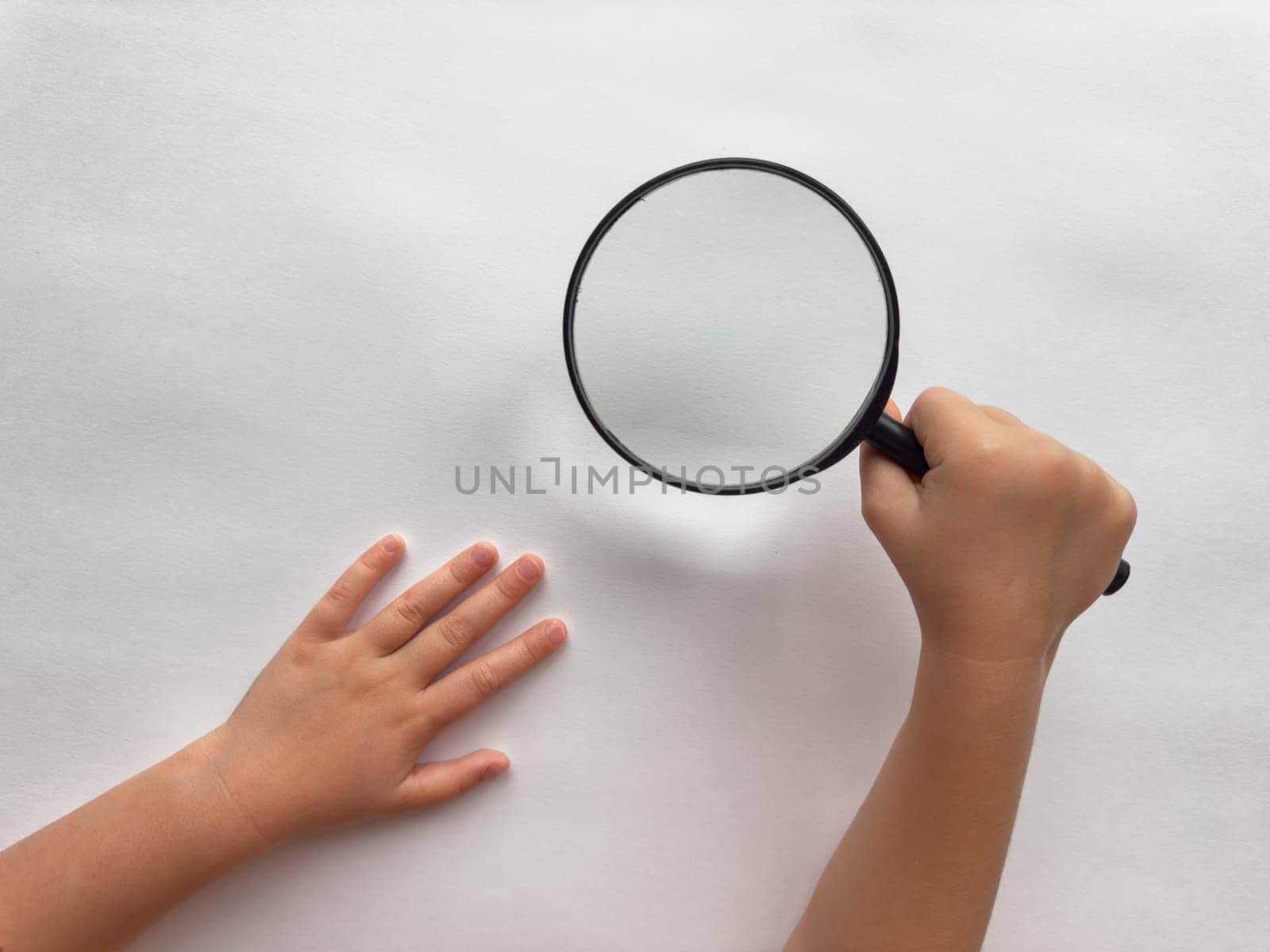 Childs curiosity. Hand holding magnifying glass over white surface.