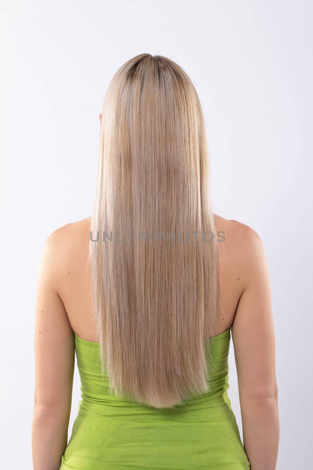 A stylish woman showcases her long hair from the back in a vibrant green dress that highlights her personality