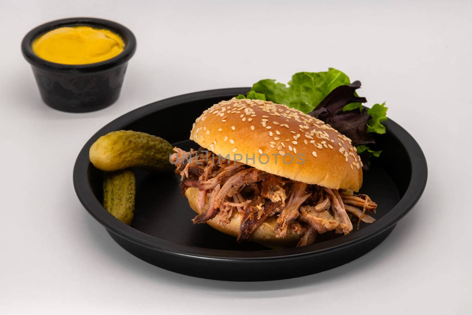 A delicious and mouthwatering pulled pork sandwich that is expertly served with crunchy pickles and a tangy mustard dip