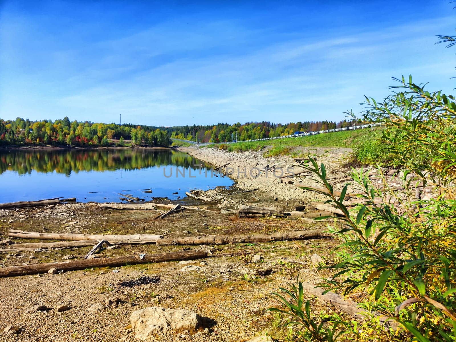 A serene lake stretches out beneath a blue sky with scattered clouds, framed by a grassy hillside.