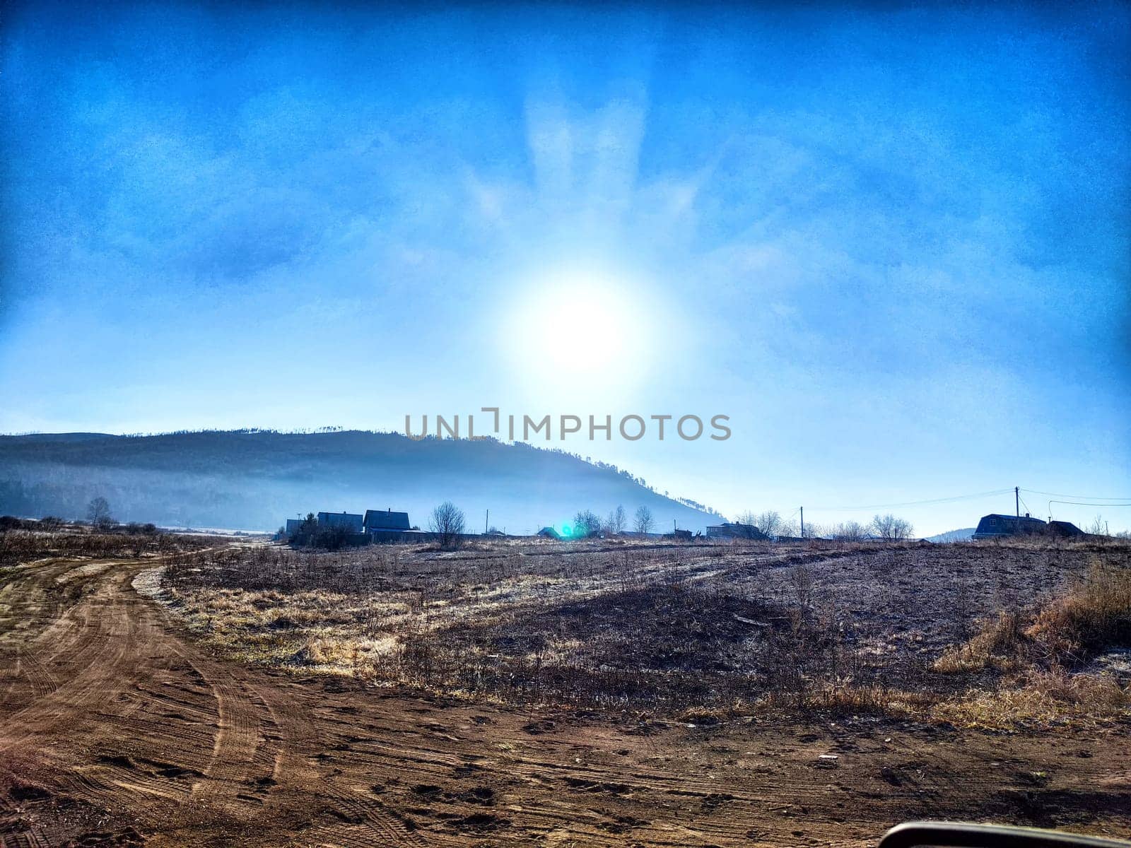 The sun rises gently, illuminating the serene countryside landscape featuring distant hills and scattered homes in the morning light.