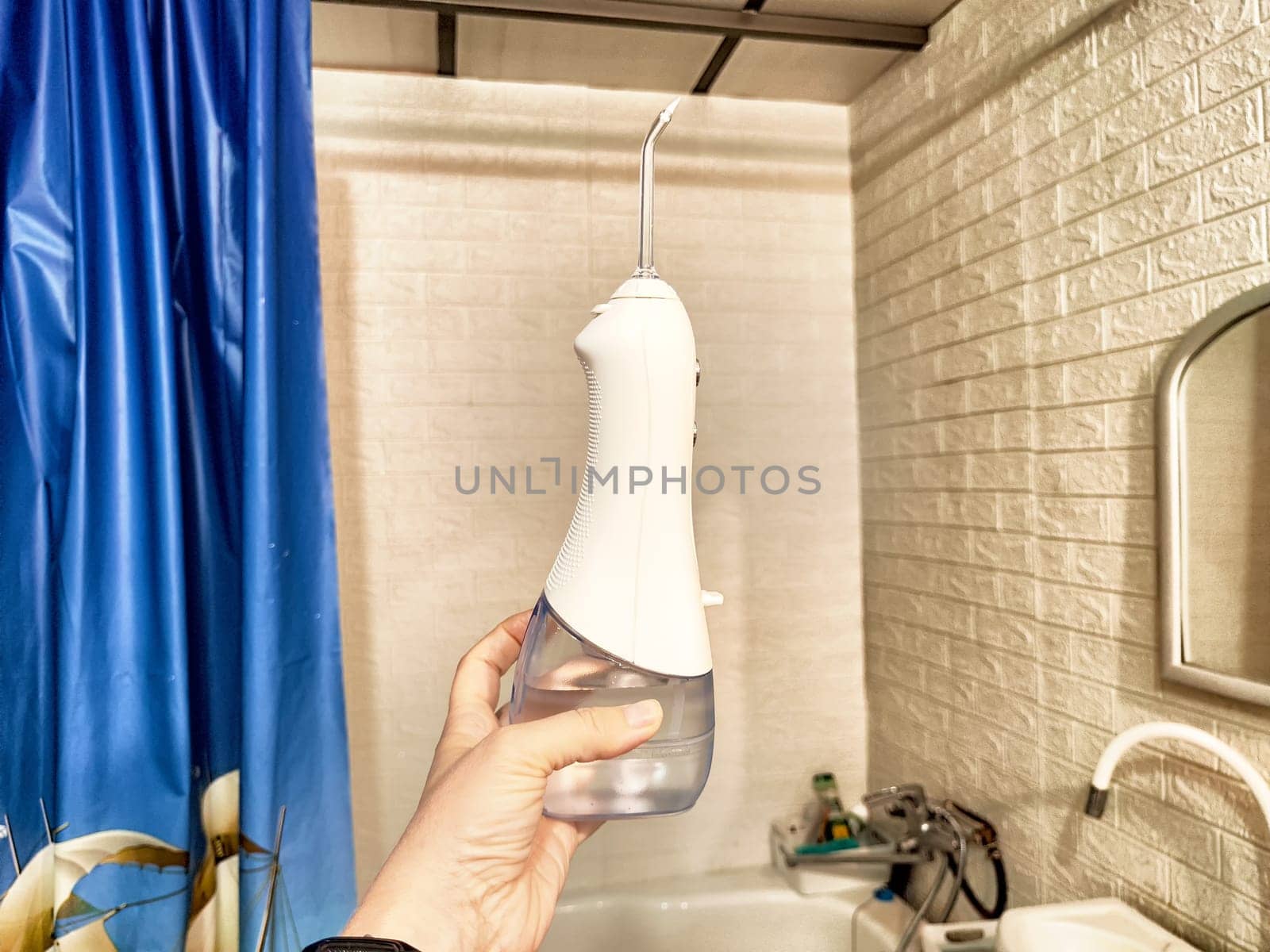 A hand grips a dental irrigator designed for oral hygiene, displayed in a bright bathroom environment with relevant accessories.