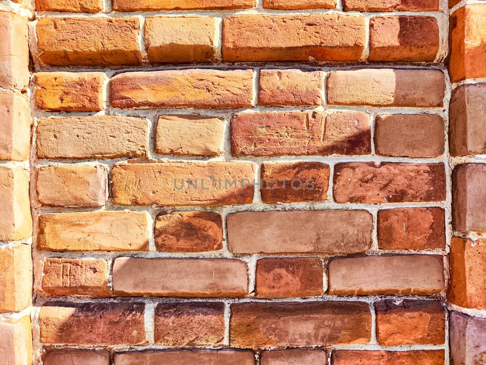 Rustic red bricks form a textured wall, displaying color variations and natural patterns under bright sunlight.