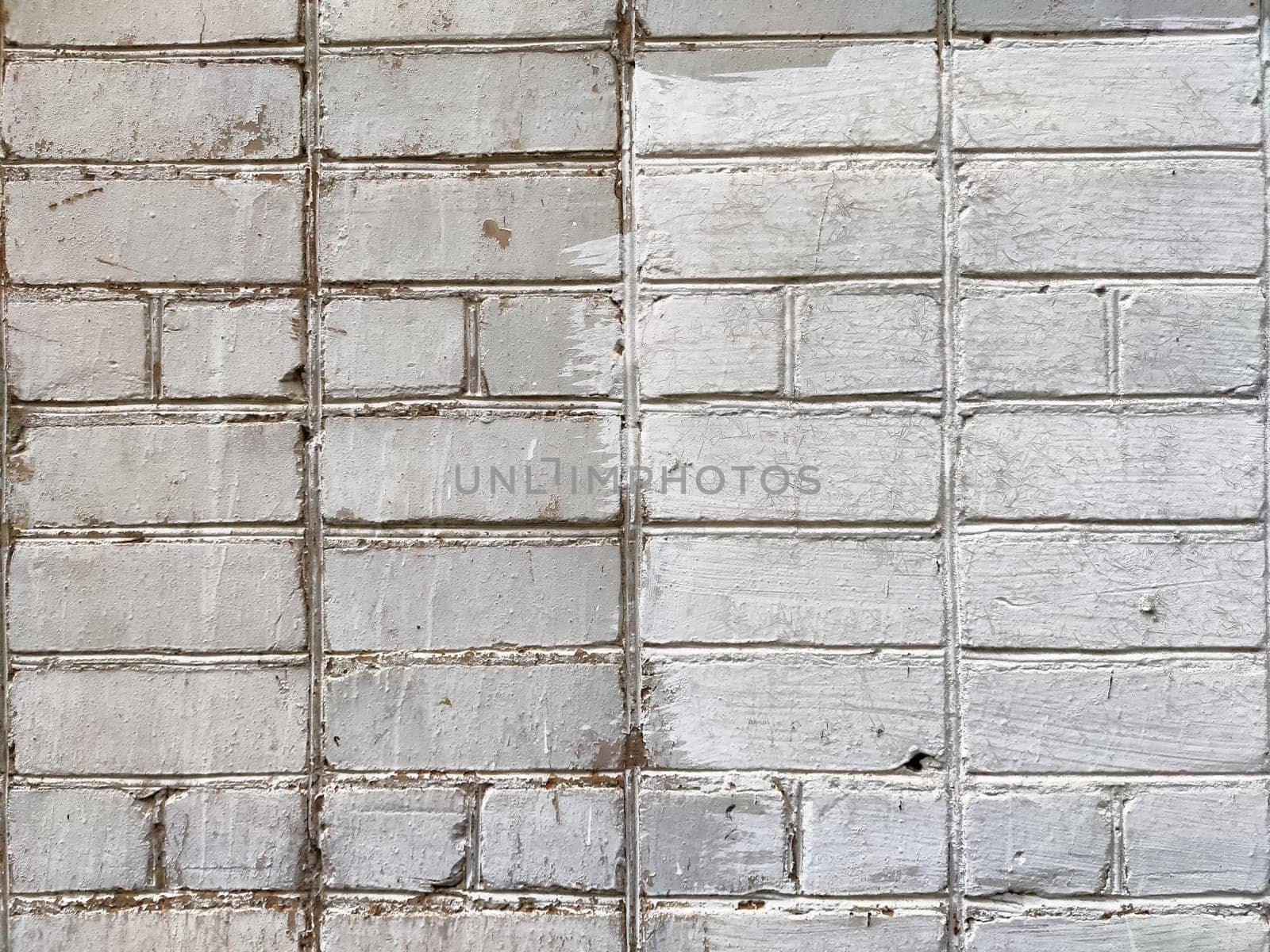 The textured surface of a brick wall displays contrasting areas of white paint wear, highlighting its age and character.