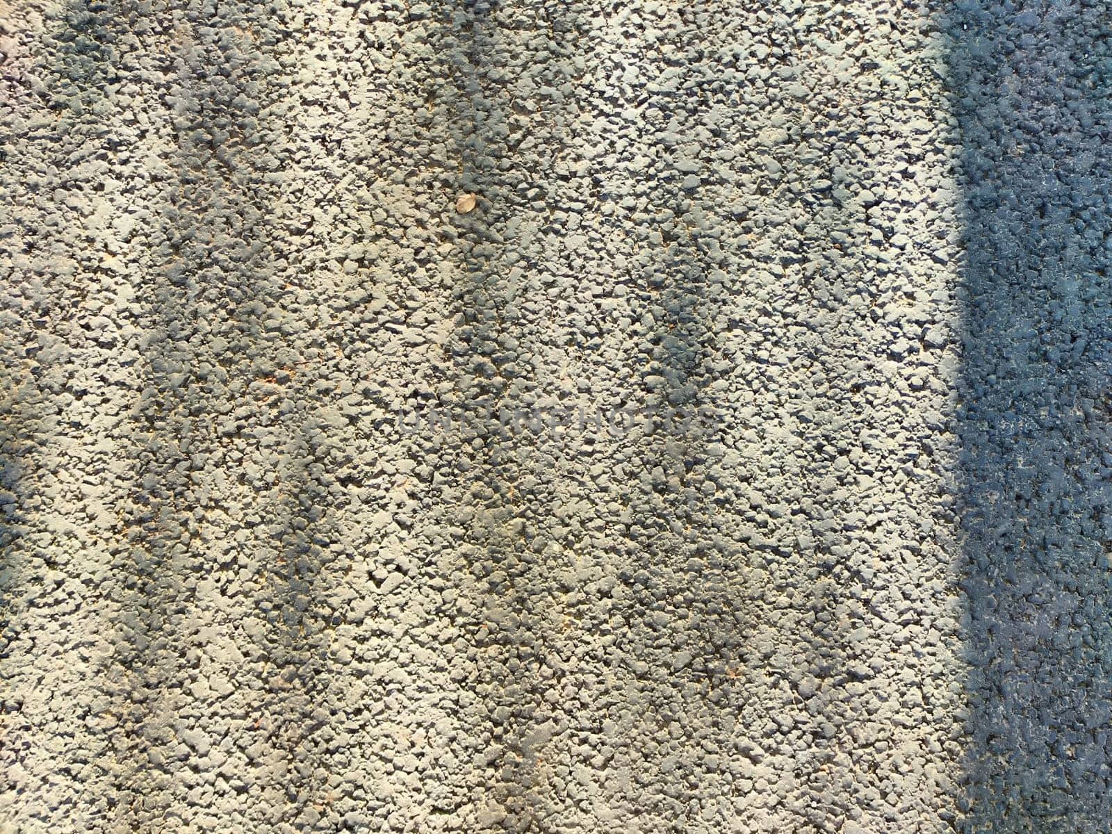 Bright daylight reveals a textured surface marked with varying shades and patterns from overlapping shadows in an outdoor area.