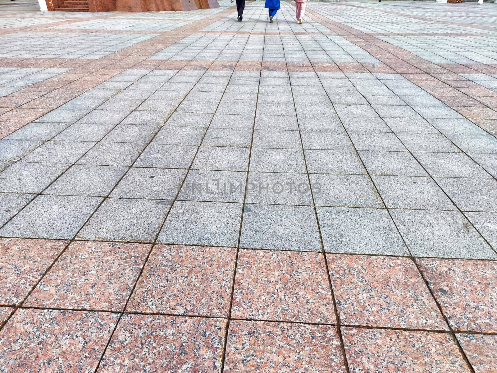 Two individuals walk across a large stone pavement in an open plaza, enjoying a sunny day in the city environment.