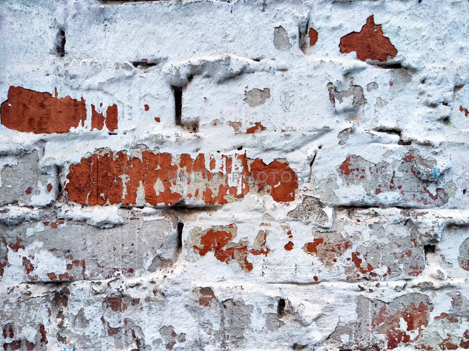 A brick wall shows signs of peeling paint with red and white hues in an urban environment.